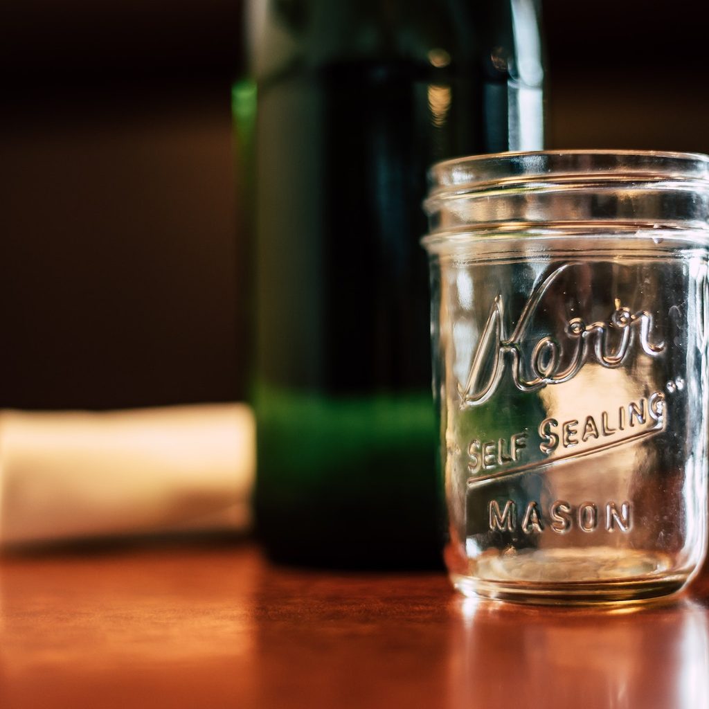 empty mason jar next to bottle and napkin
