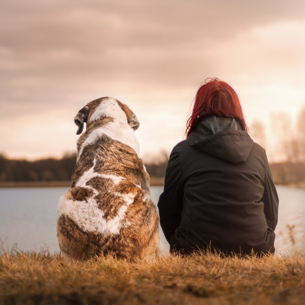 A girl and her dog sitting together in front of a lake