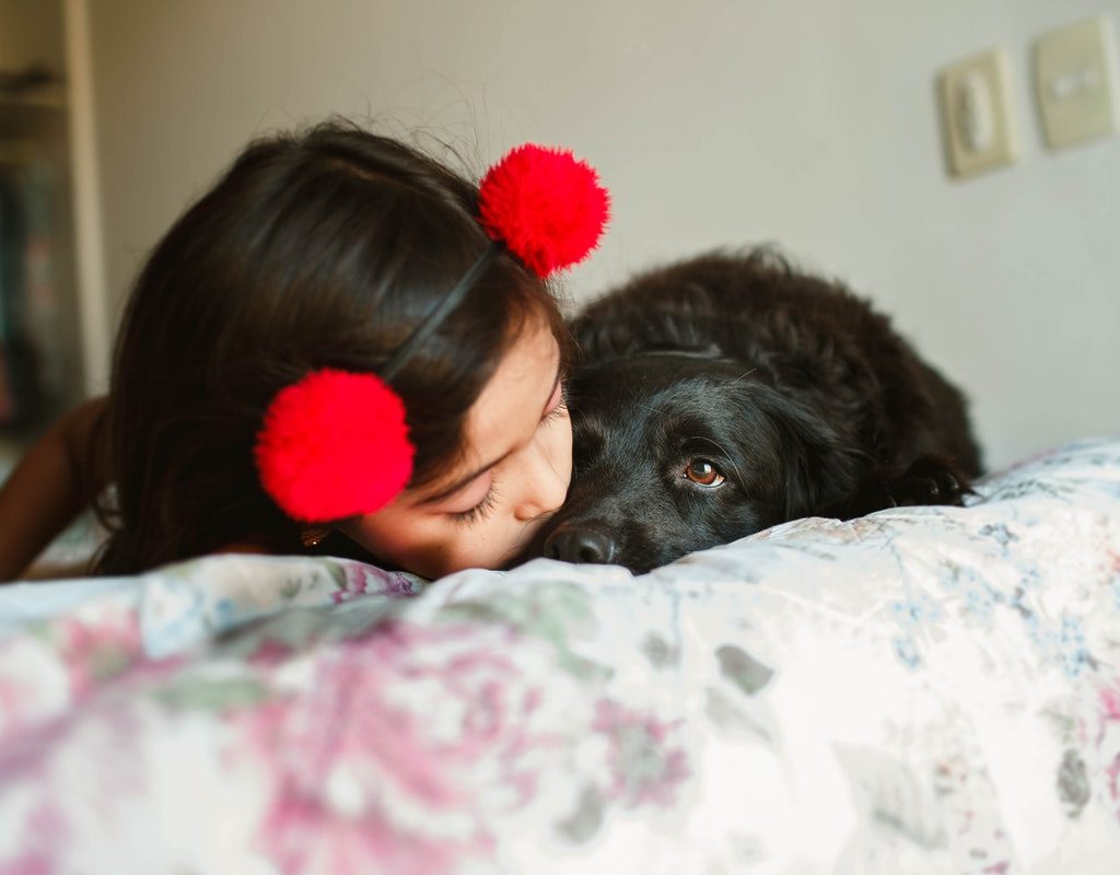 A young girl and her puppy cuddling on a bed