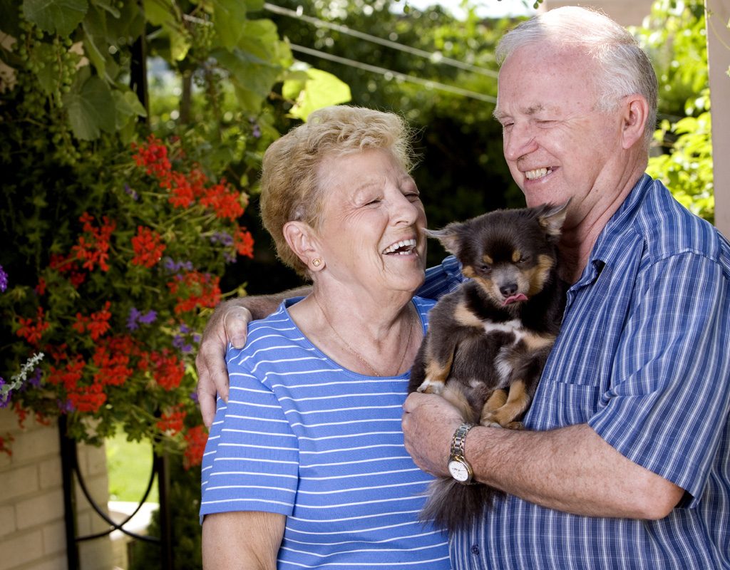 Older man and woman holding small dog.