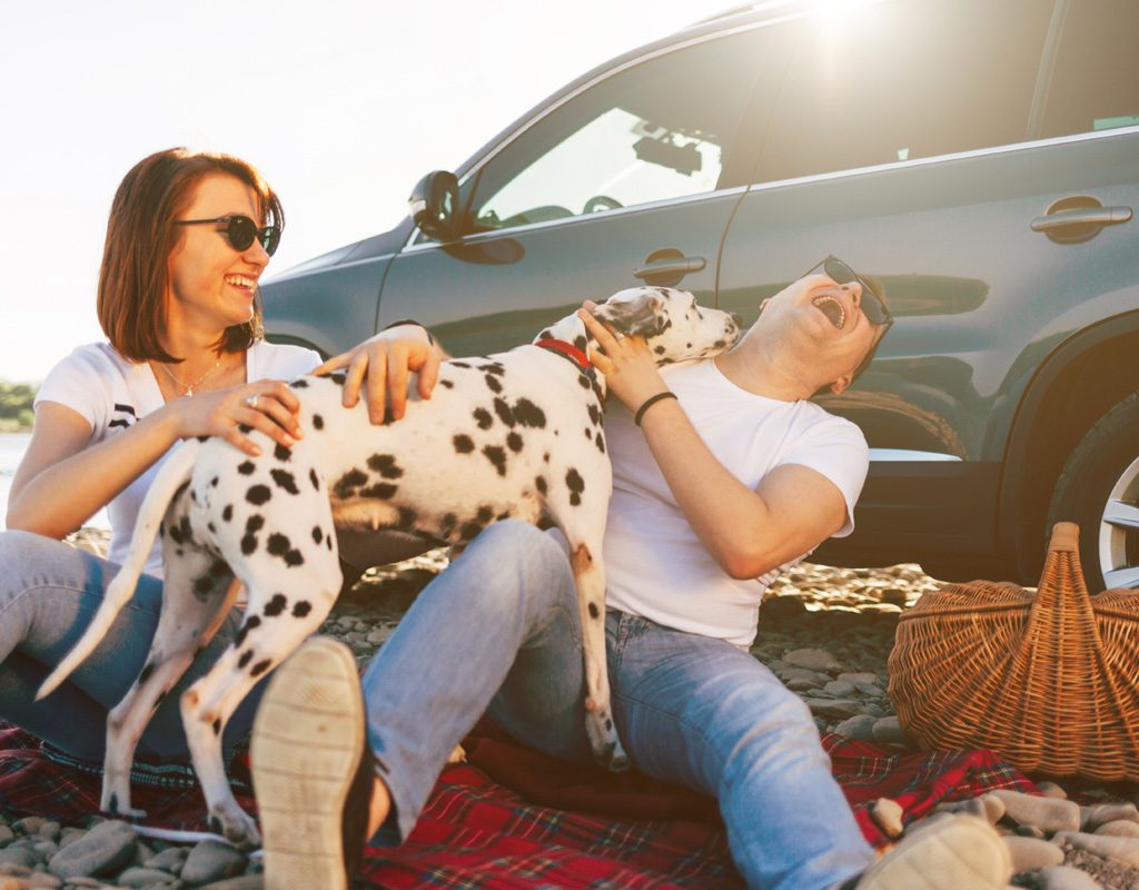 Woman and man having fun with a dog on a road trip.