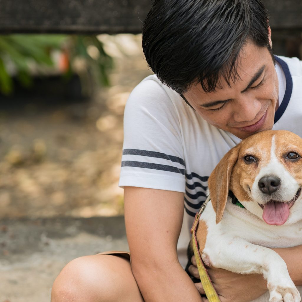 A man hugs and pets his beagle somewhere outside