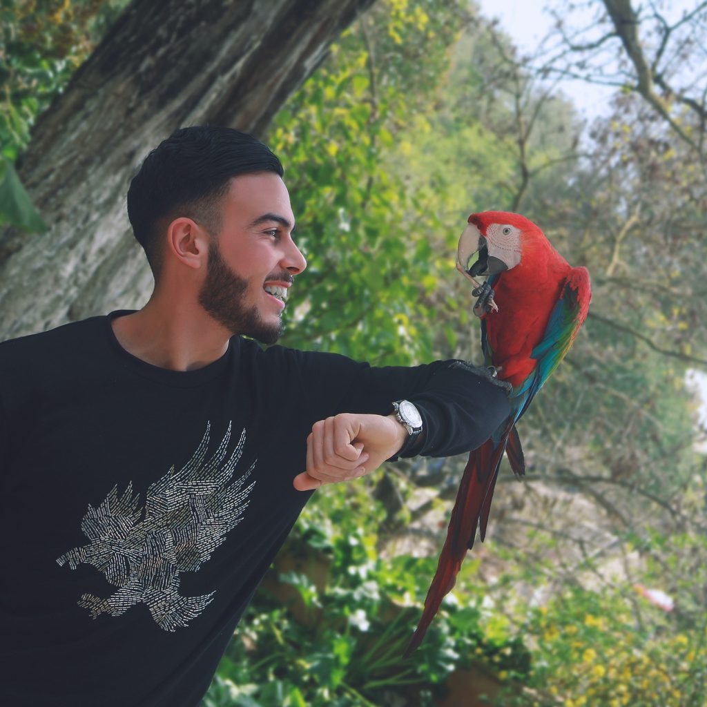 Man stands outside with a parrot on his arm