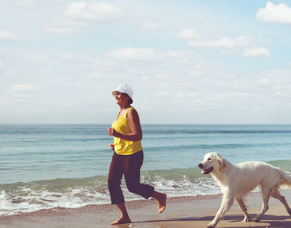 Mature woman running on beach with dog.