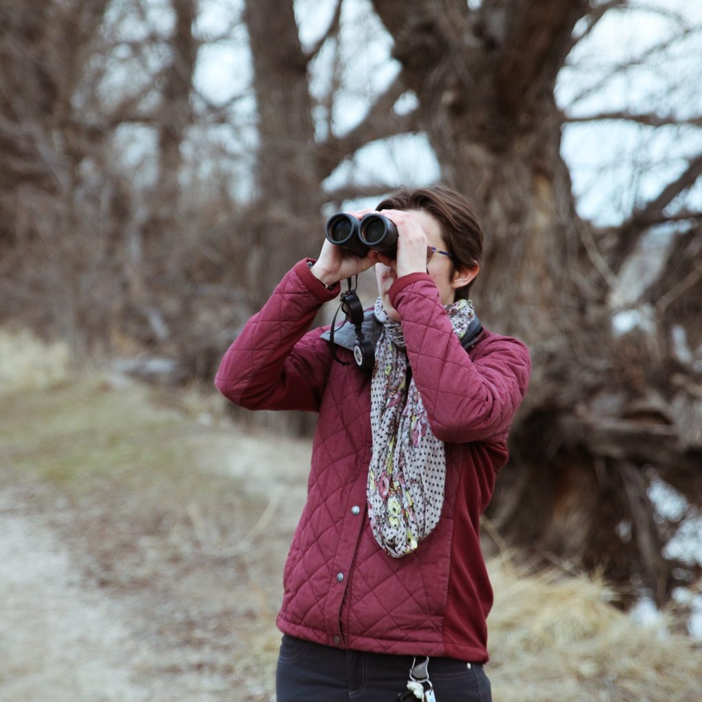 Woman looks through binoculars at a bird