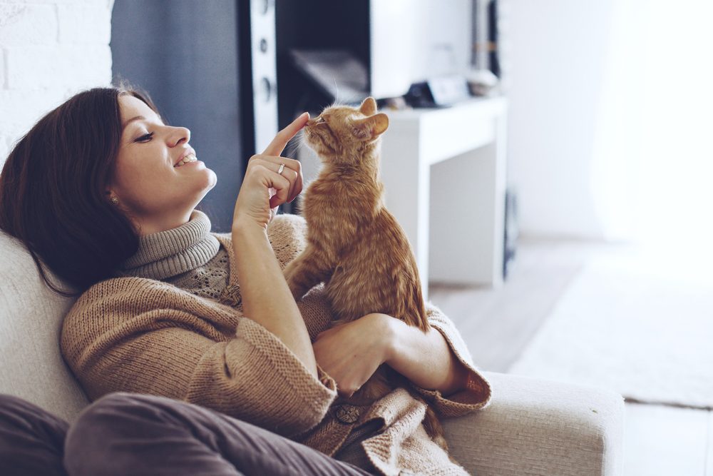 A woman wearing a beige sweater holding an orange tabby kitten.