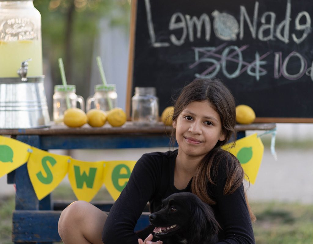 Young girl with puppy at lemonade stand.