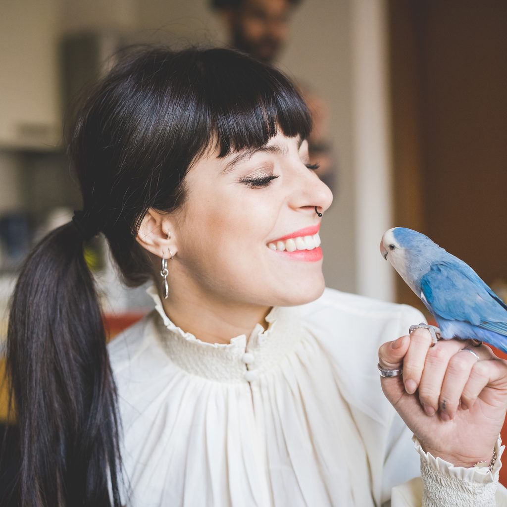 Woman smiles at her pet bird perched on her finger