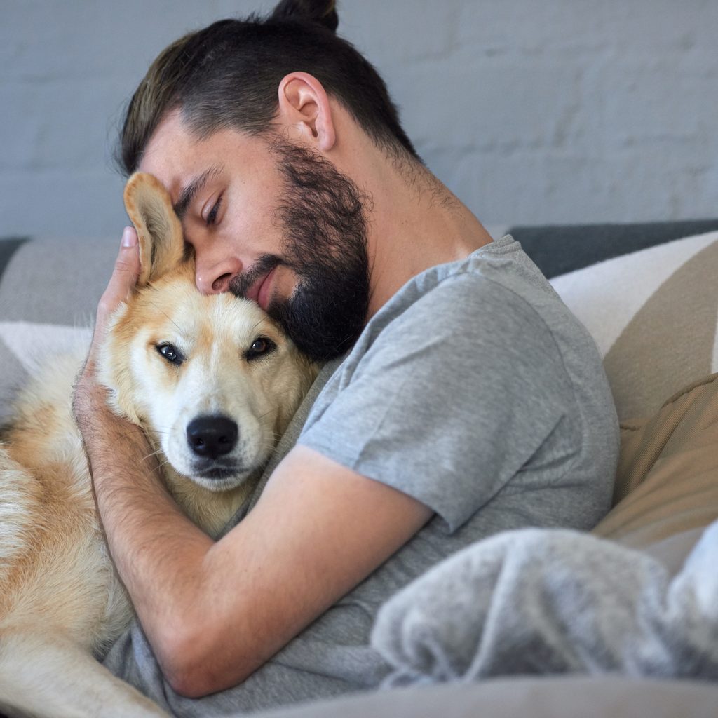 A man hugs his dog on the couch.