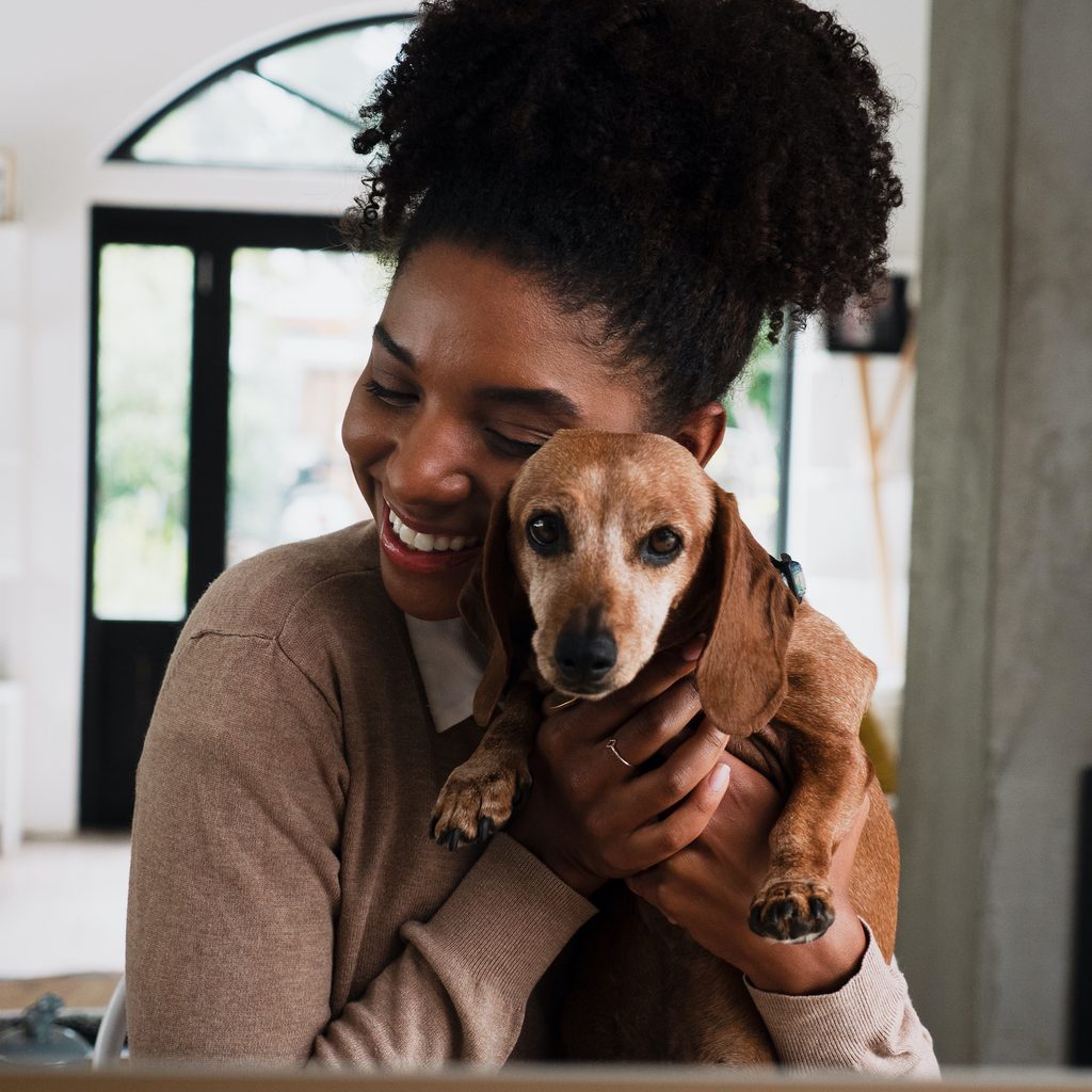 A woman hugs her Dachshund dog in her home