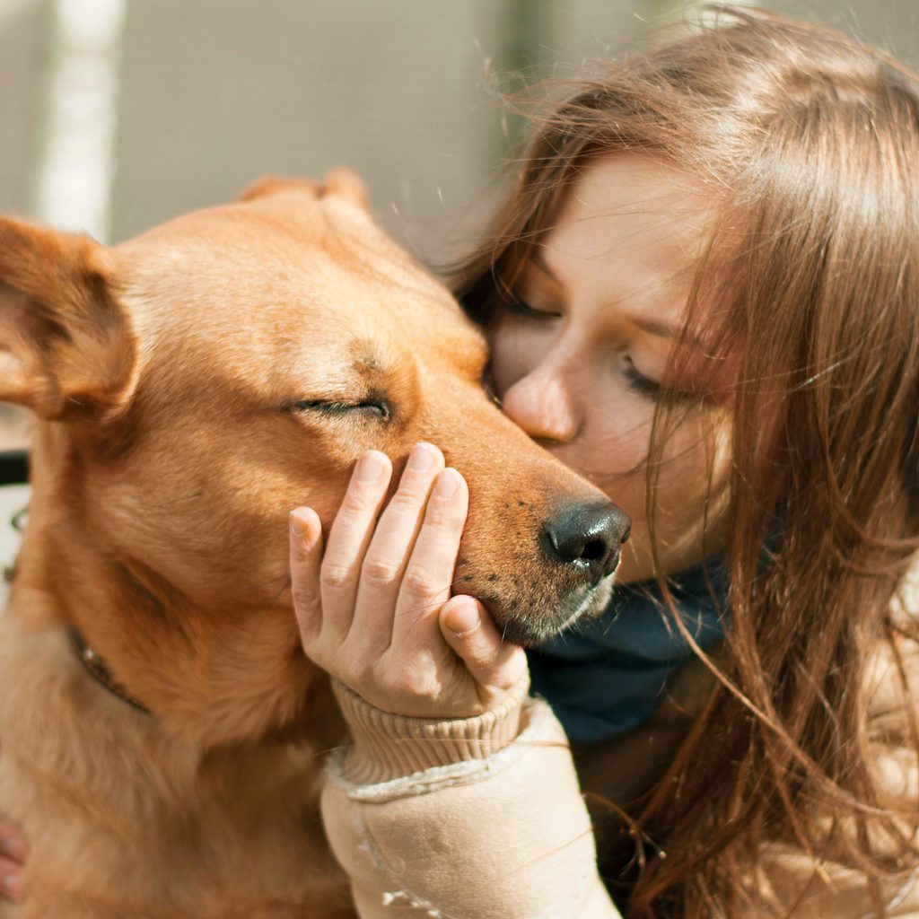 A woman holds and kisses her dog