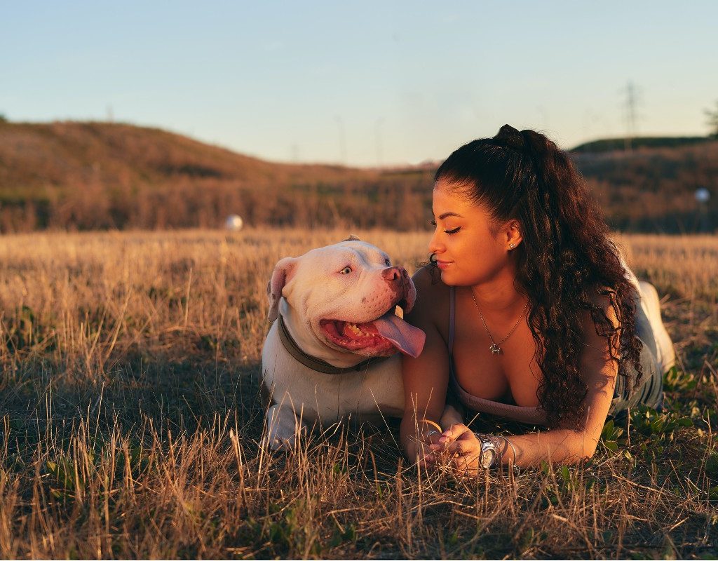 a woman sitting in the grass with her pit bull