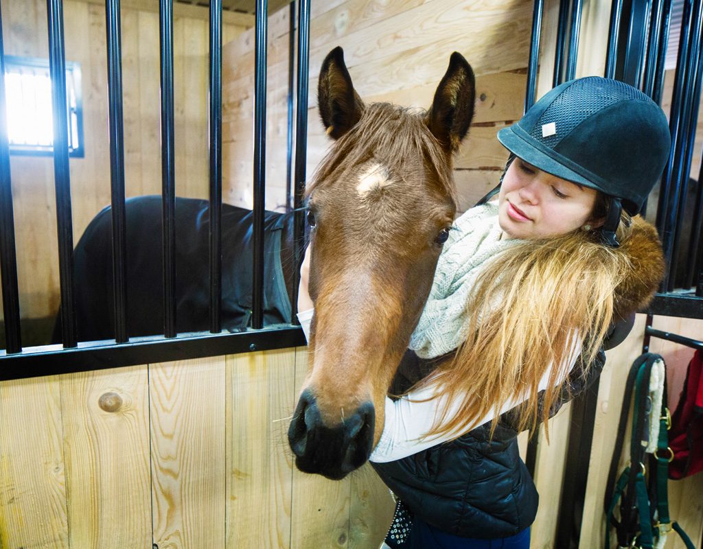 A young girl hugs a horse in the stables.