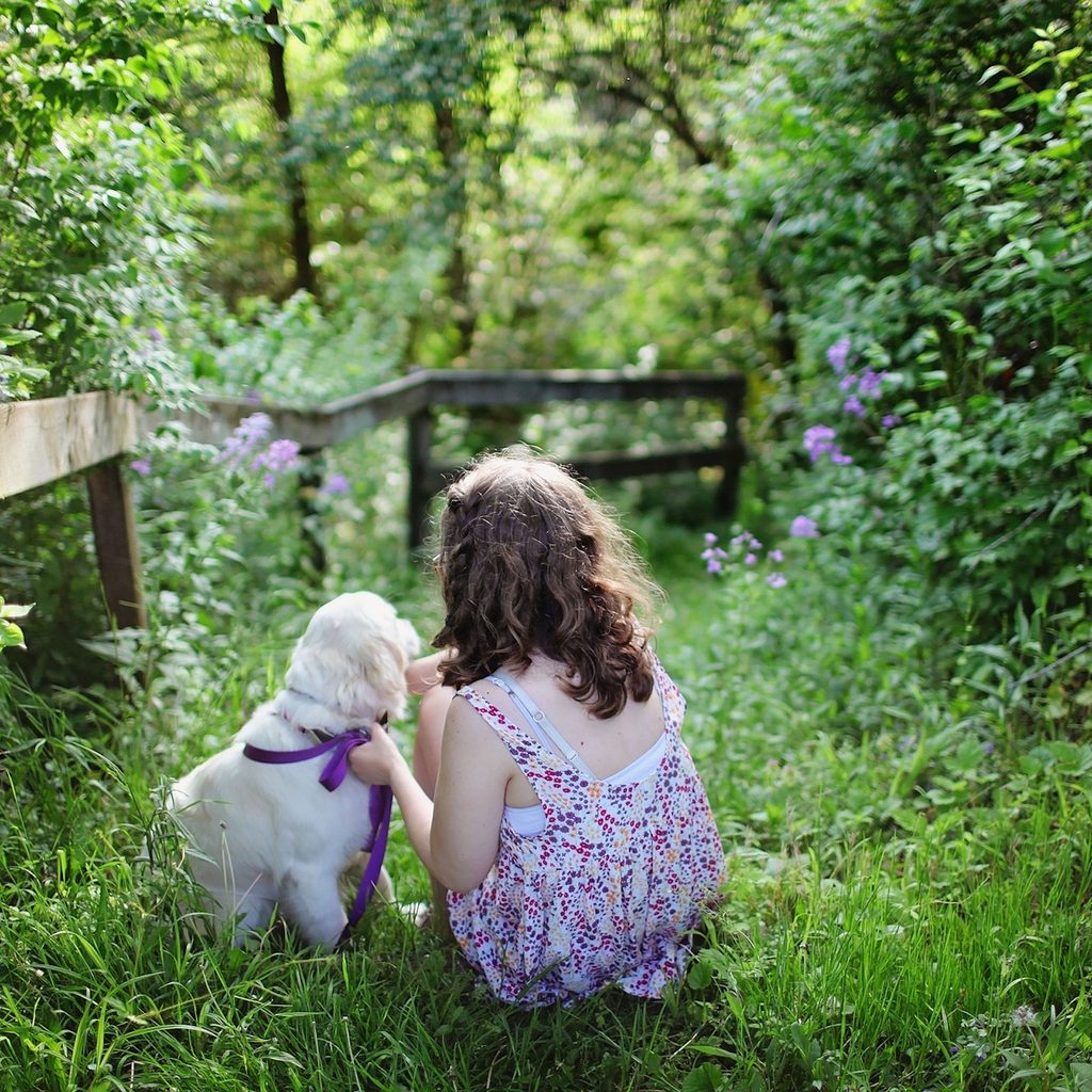 A little girl and a puppy sit on the grass in a lush green outdoor area