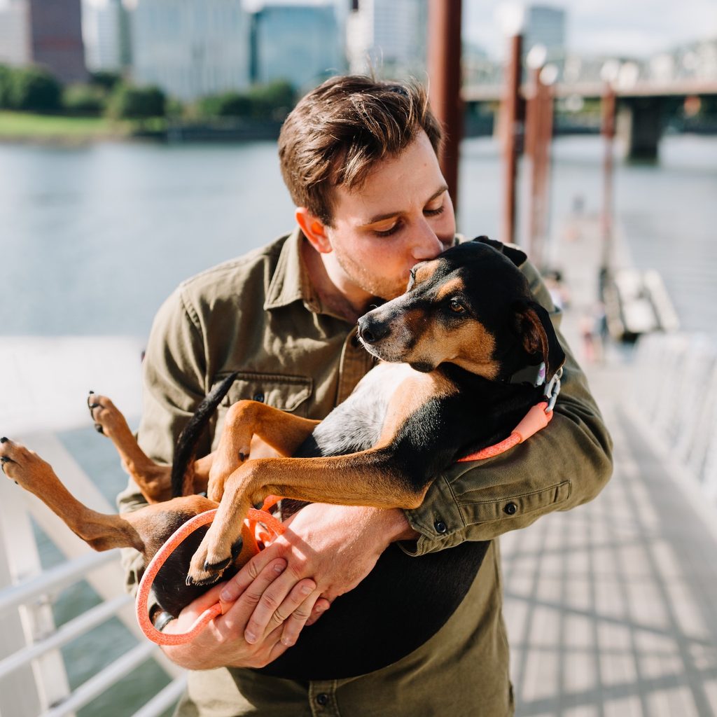 A man dressed in a Jacket holds his black and brown dog in his arms and kisses the dog