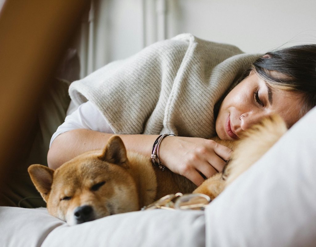 Woman in sweater and dog napping on couch