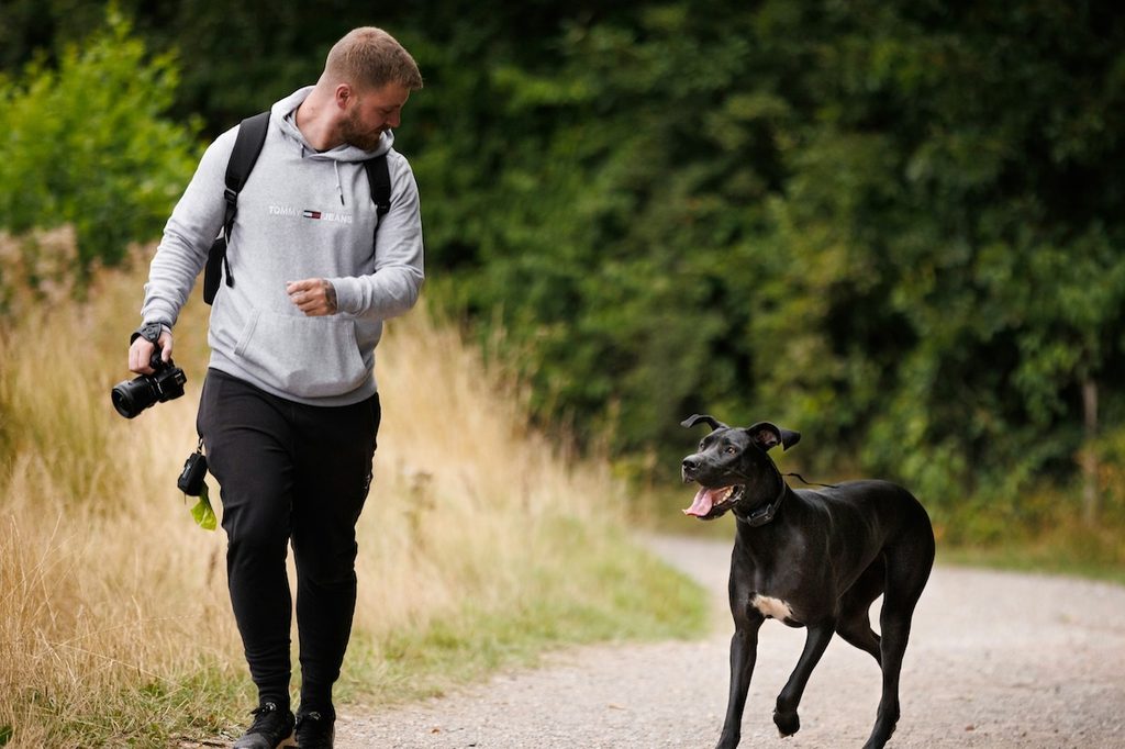 man with camera running on road with large black dog who is off leash and panting