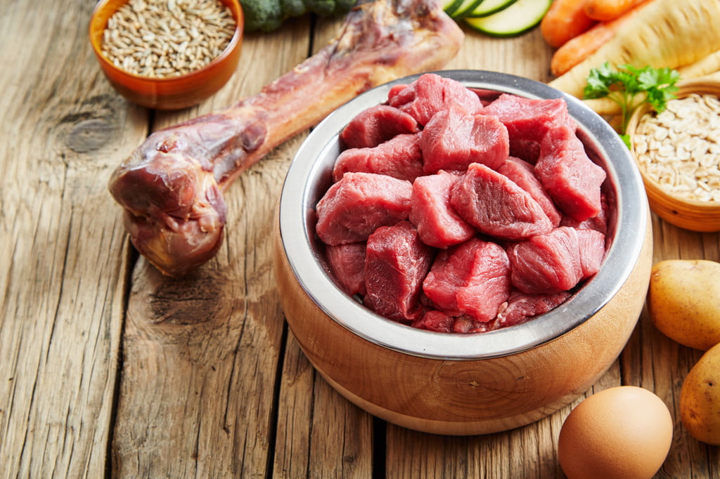 A bowl of raw meat on a table surrounded by raw ingredients