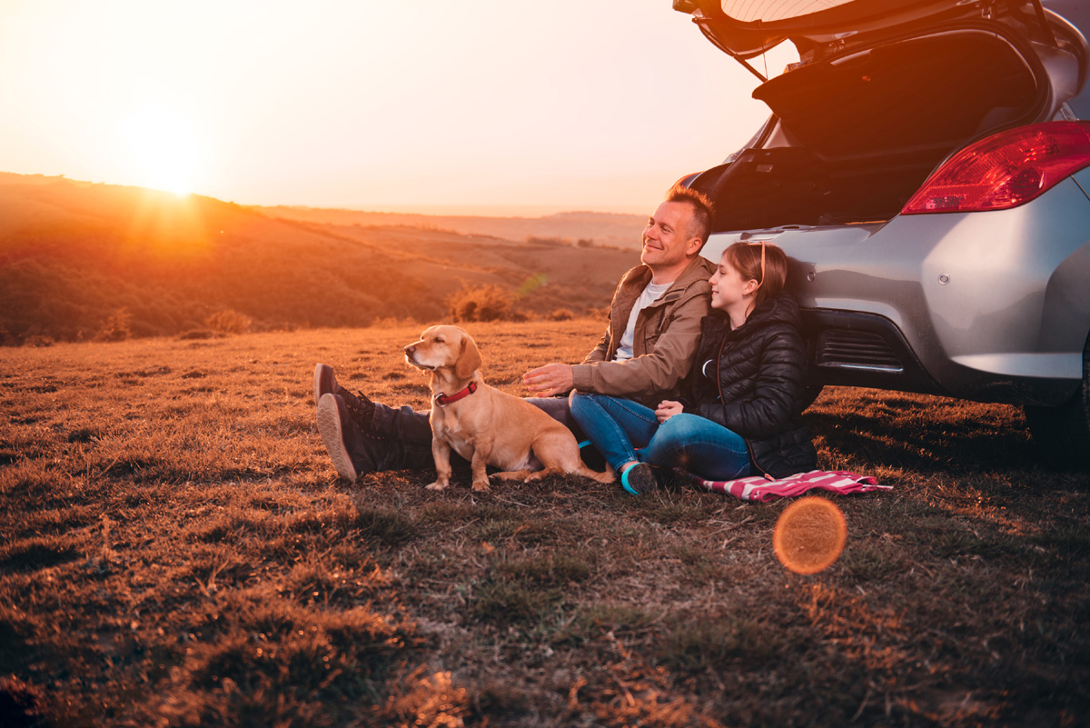 man, girl and dog sitting beside a car