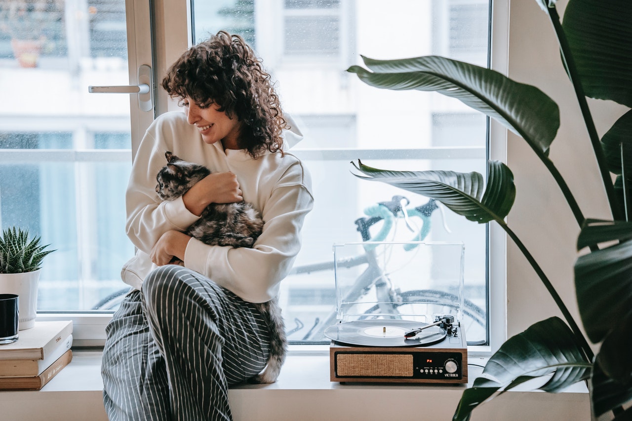 A woman sitting on a windowsill holding a calico cat.