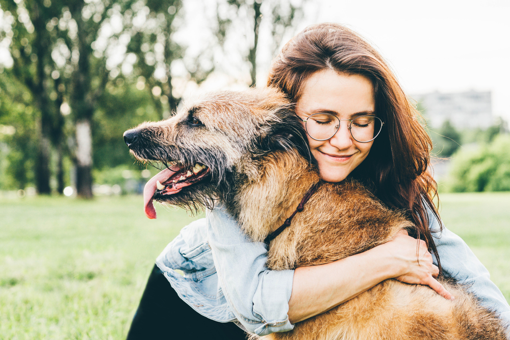 A woman in glasses holding an old brown dog.