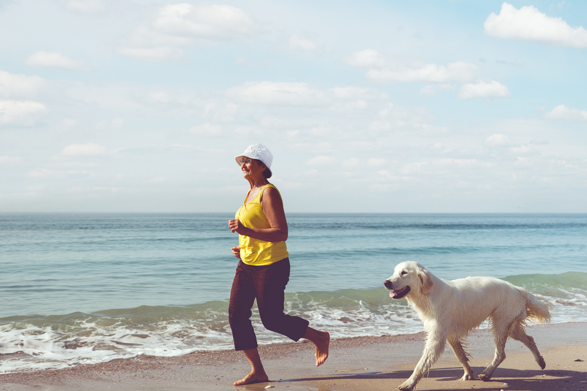 Mature woman running on beach with dog.