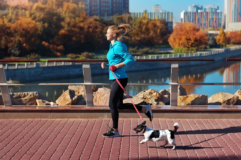 Moteris bėgioja su terjeru.