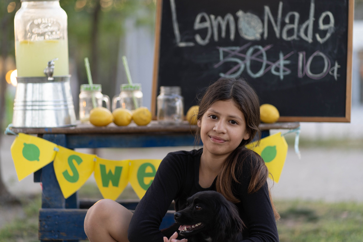 Young girl with puppy at lemonade stand.