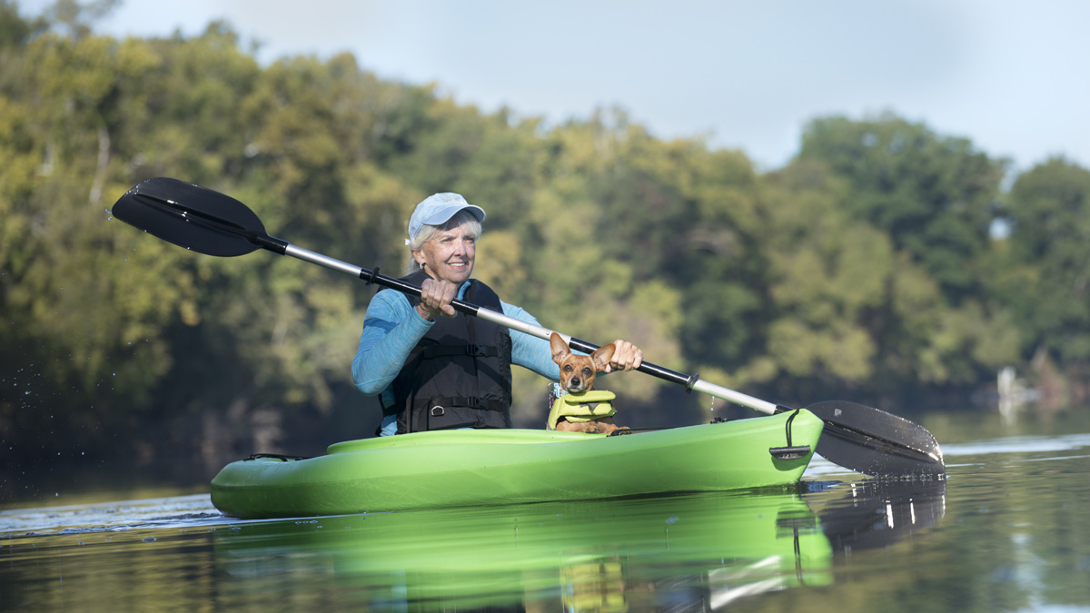 Woman kayaking on lake with a small dog.