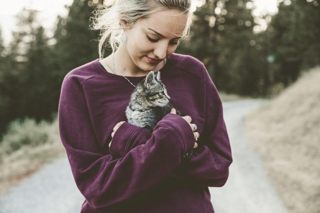 Šviesiaplaukė moteris, vilkinti purpurinį megztinį, rankose laiko kačiuką.