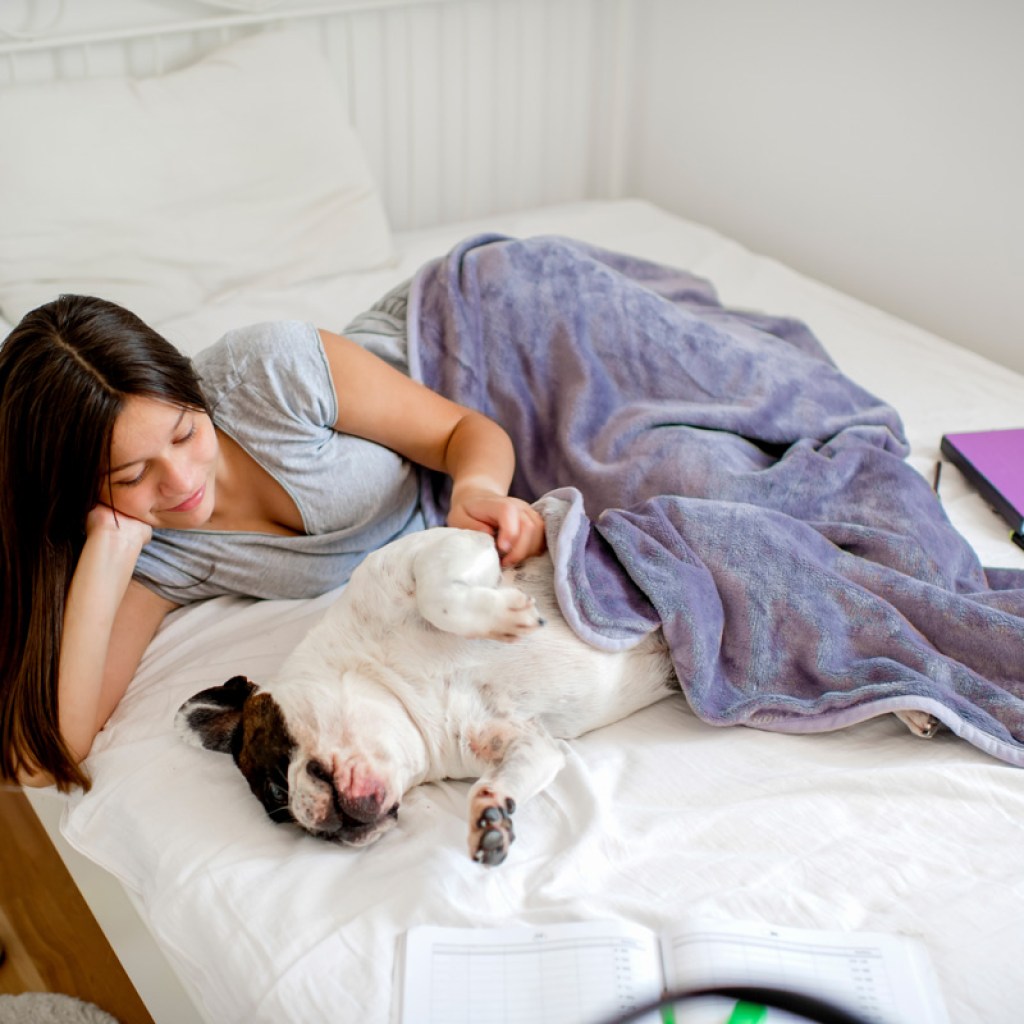 Teenage girl cuddling with dog on bed.