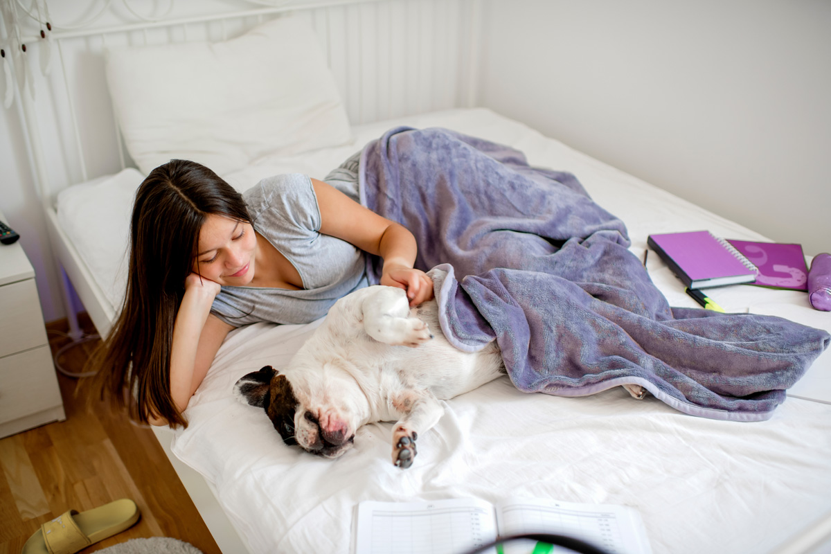 Teenage girl cuddling with dog on bed.