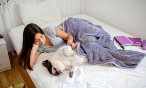 Teenage girl cuddling with dog on bed.