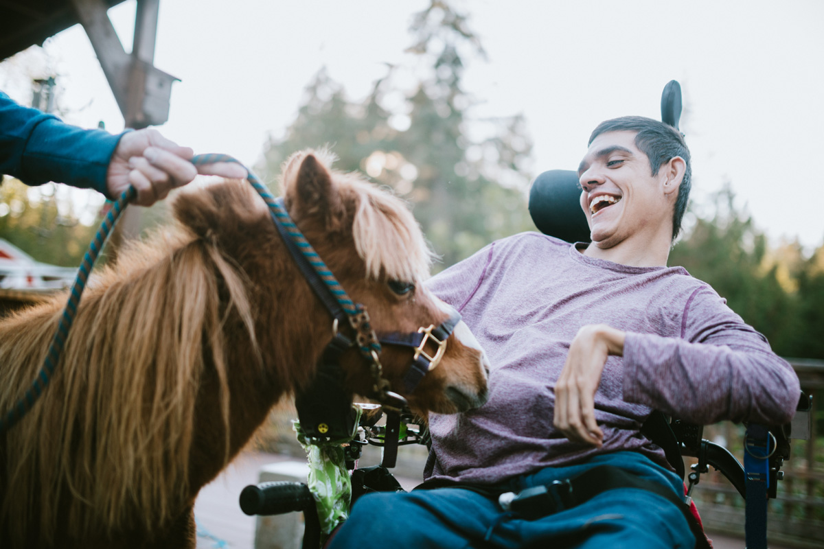 Man in a wheelchair laughing as he pets a horse.