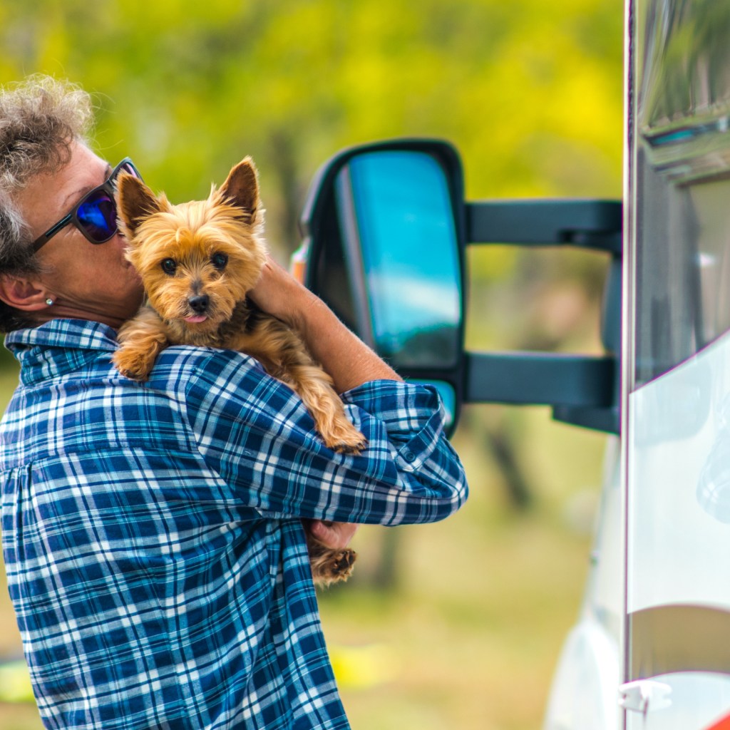 A person hugs and kisses their Yorkshire Terrier outside of an RV