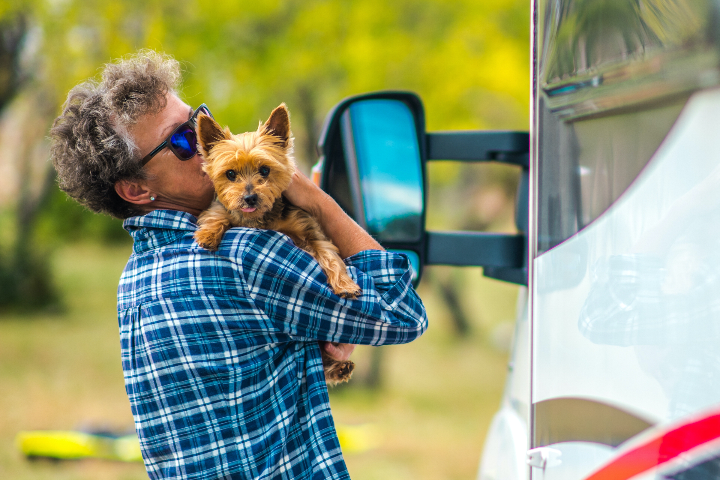 A person hugs and kisses their Yorkshire Terrier outside of an RV