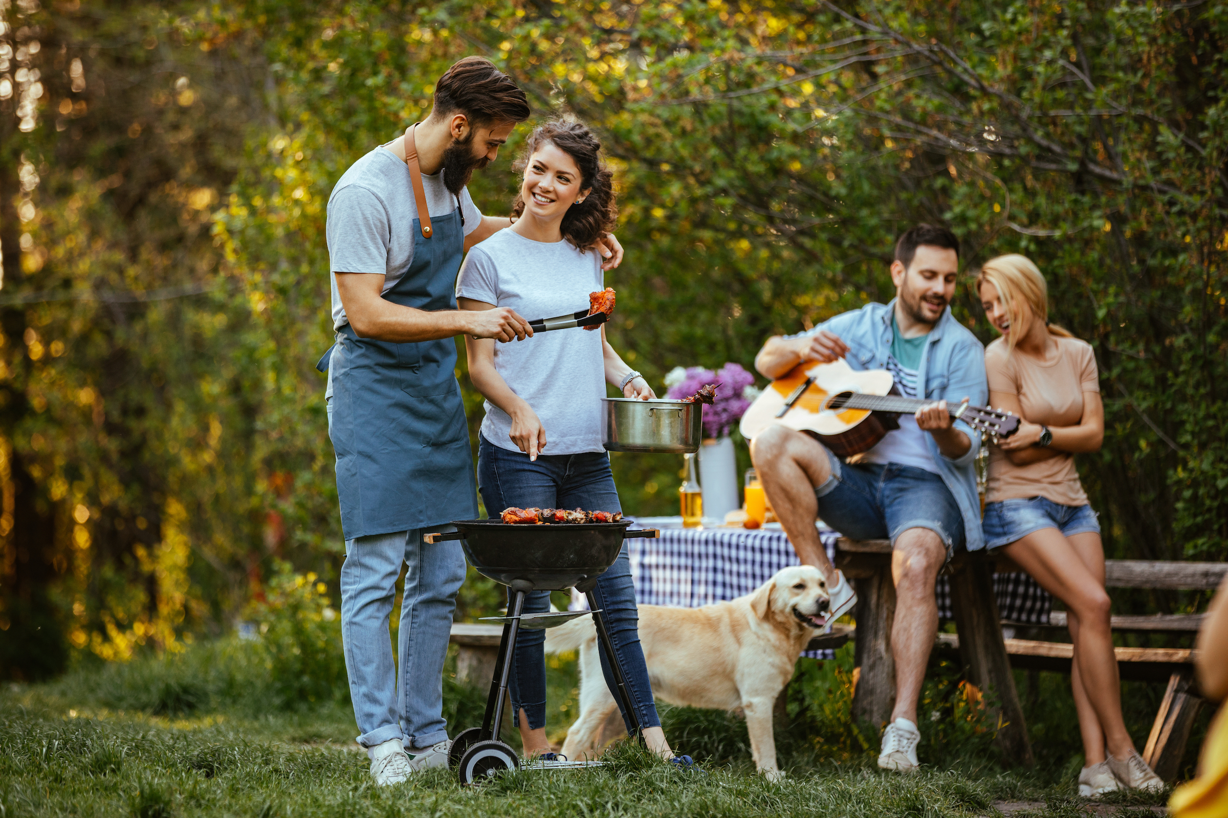 Two couples prepare a barbecue while a Golden Retriever watches on