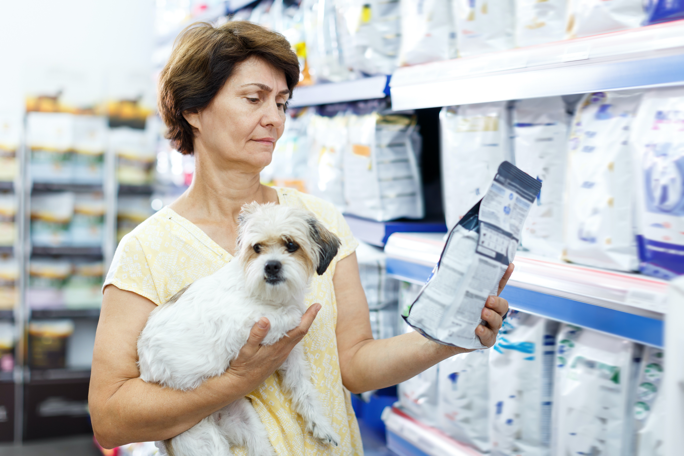 A woman holds her dog and reads a bag of dog food at the pet store