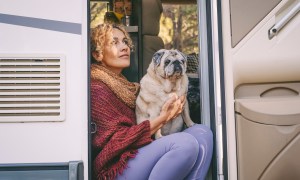 A woman sits on the step of an RV holding a Pug on her lap