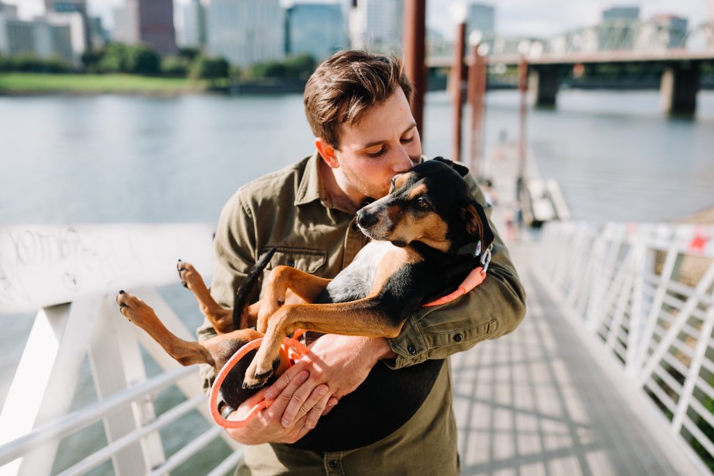 A man dressed in a Jacket holds his black and brown dog in his arms and kisses the dog