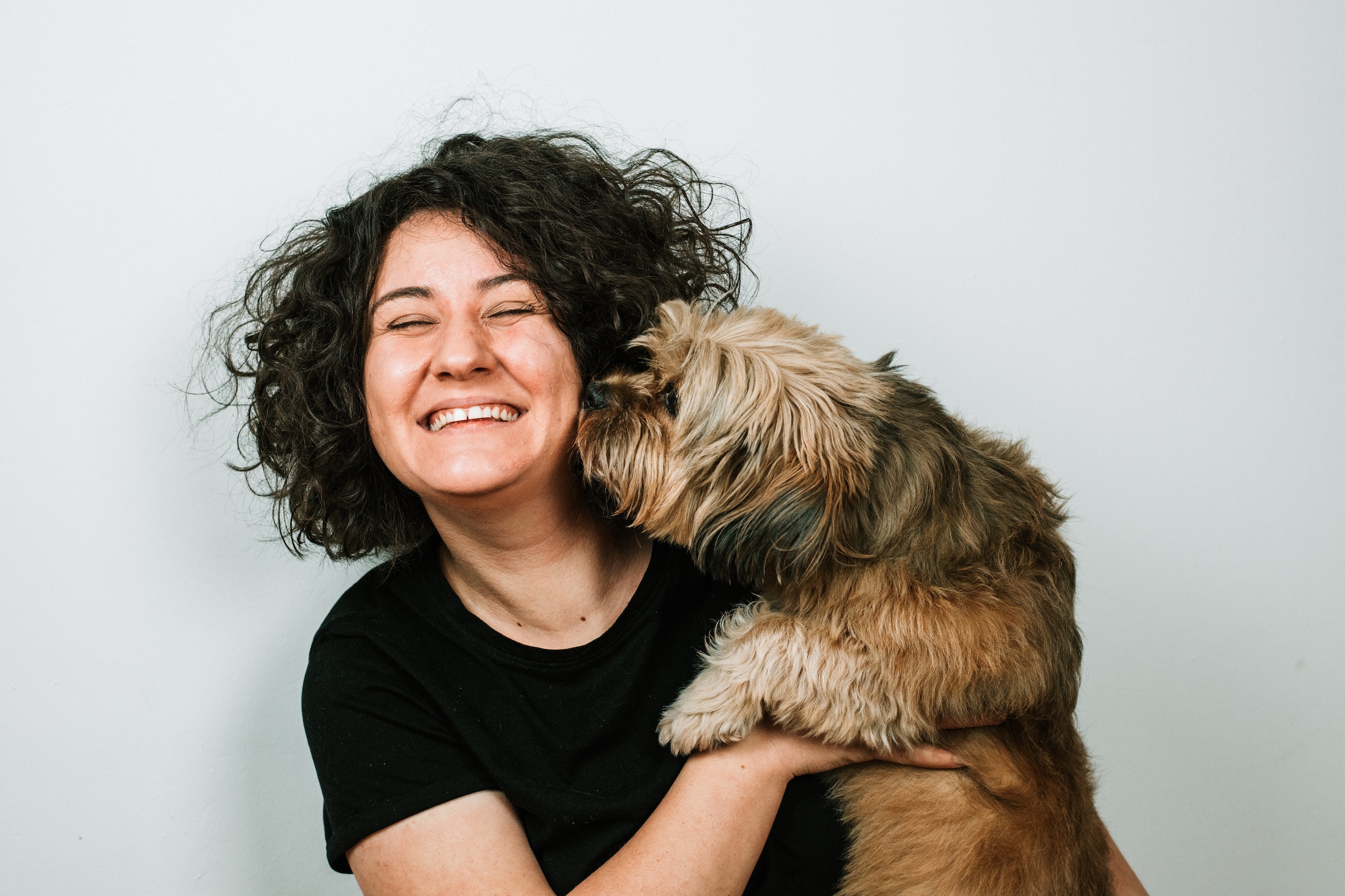 A woman hugs her small, brown dog and laughs as the dog sniffs her face