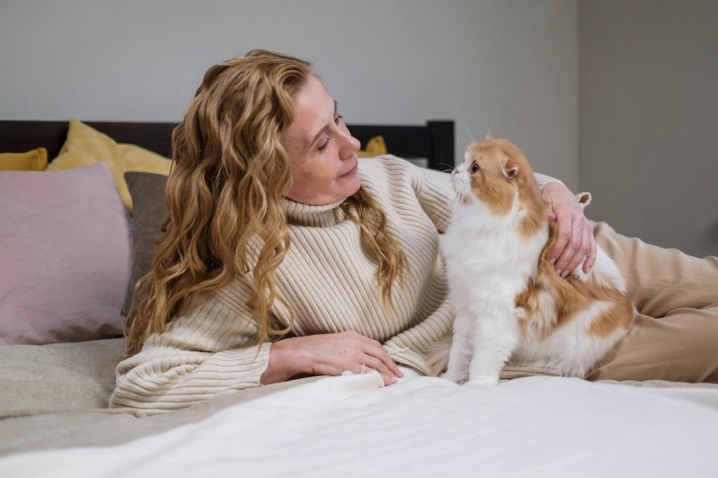A woman lies in bed petting her cat