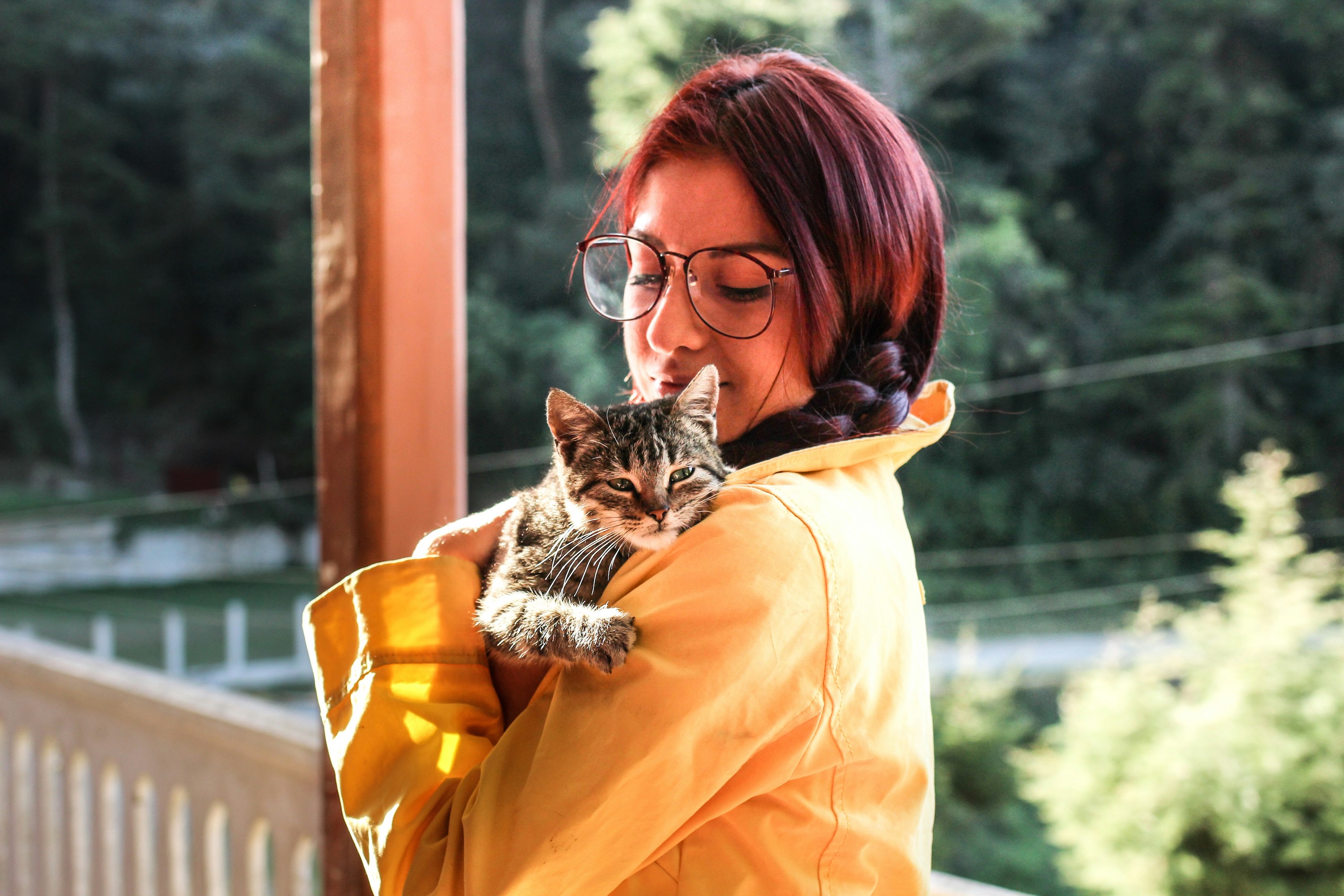 A woman wearing a yellow jacket holds a tabby cat while standing outside