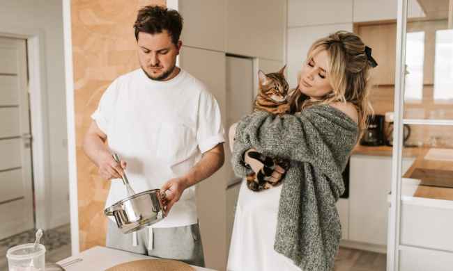 Pregnant woman holding a cat in the kitchen with a male partner